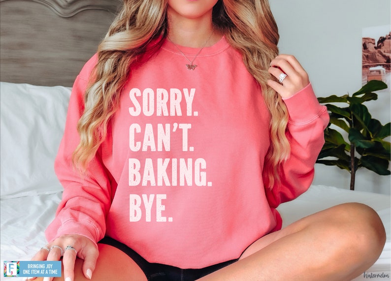 May include: A pink sweatshirt with the text "SORRY. CAN'T. BAKING. BYE." in white.