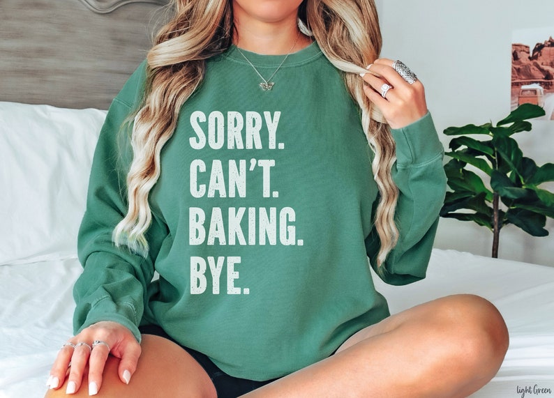 May include: A light green sweatshirt with the text "SORRY. CAN'T. BAKING. BYE." printed in white.
