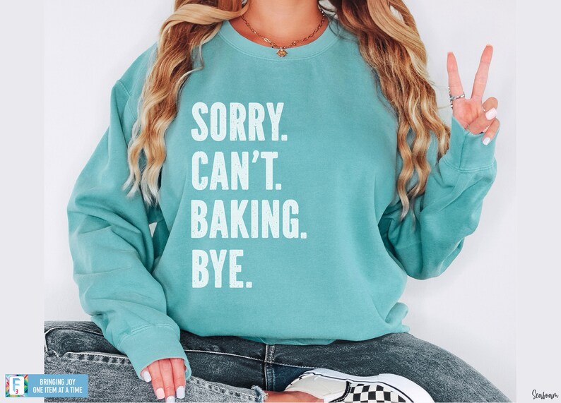 May include: A teal blue sweatshirt with the text "SORRY. CAN'T. BAKING. BYE." in white.