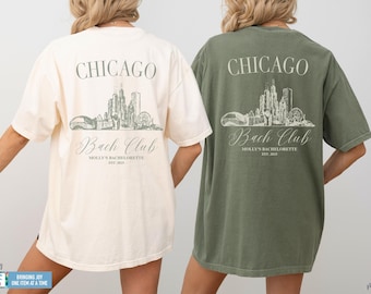 May include: Two short-sleeve t-shirts, one ivory and one moss green, featuring a back graphic of the Chicago skyline. The text reads CHICAGO, Bach Club, MOLLY'S BACHELORETTE, and EST. 2025. The design is printed in a muted tone on the back of each shirt.
