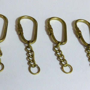 May include: Four gold-toned keychains with oval-shaped loops and attached chains. Each keychain has a small, round ring at the end of the chain.