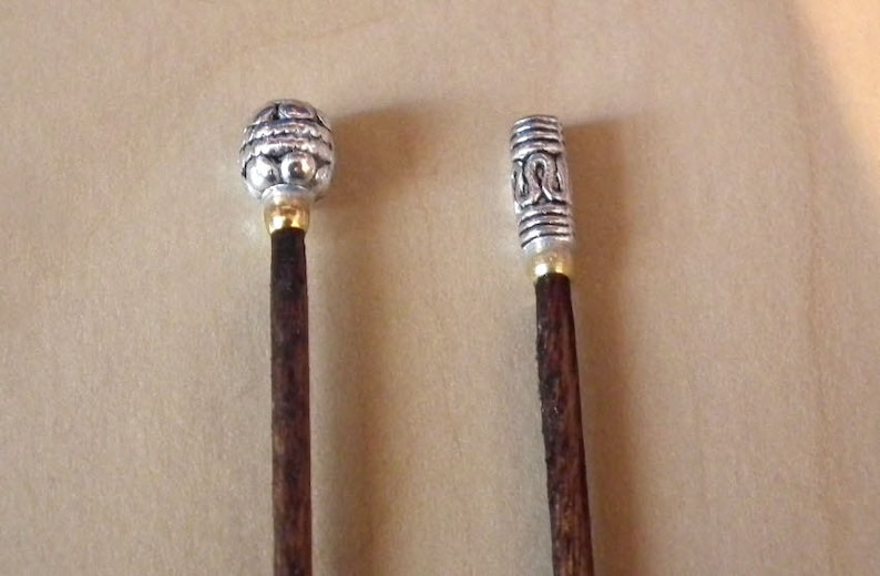 May include: Two wooden knitting needles with silver metal tips. The tips have intricate designs.