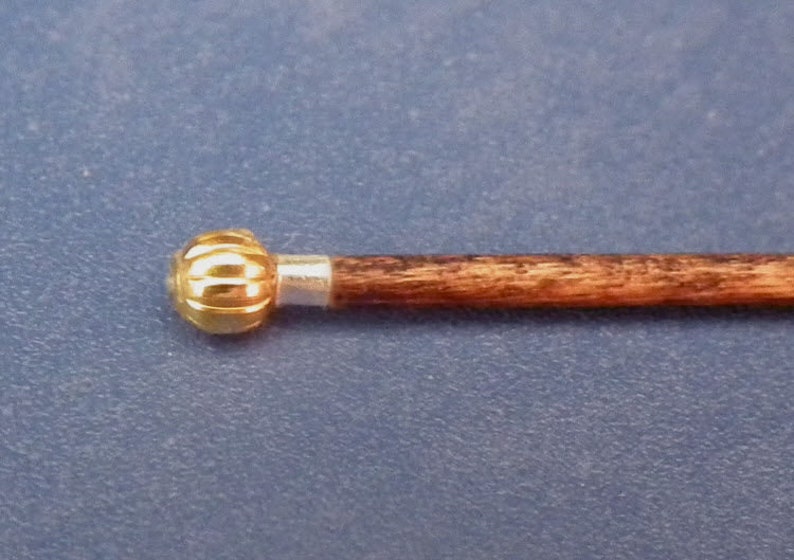 May include: A wooden walking stick with a gold-coloured knob on the end. The knob has a ribbed design.