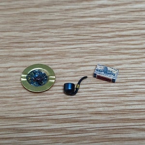 May include: A black pipe, a gold ashtray, and a matchbox with the text "Protection" on it. The matchbox has a red, white, and blue design.