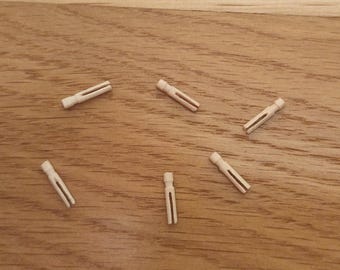 May include: Five small, light-colored wooden clothespins arranged in a scattered pattern. Each clothespin features a simple, slender design with a split body and a rounded top, showcasing the natural grain and pale beige tone of the wood.