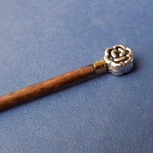 May include: A wooden stick with a silver rose-shaped topper. The stick is brown and the rose is silver with a gold accent.
