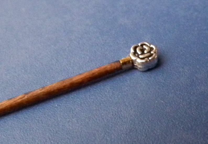 May include: A wooden stick with a silver rose-shaped topper. The stick is brown and the rose is silver with a gold accent.