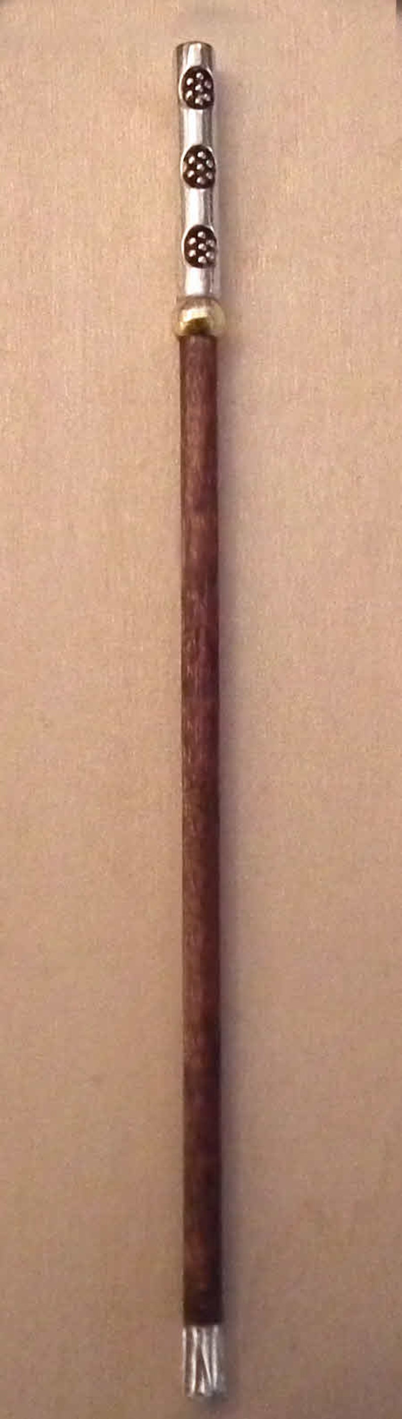 May include: A brown wooden walking stick with a silver metal top and three silver metal rings. The rings have a decorative pattern of small circles.
