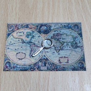 May include: A vintage world map printed on paper with a silver magnifying glass on top. The map shows the continents of North America, South America, Europe, Asia, Africa, and Australia.