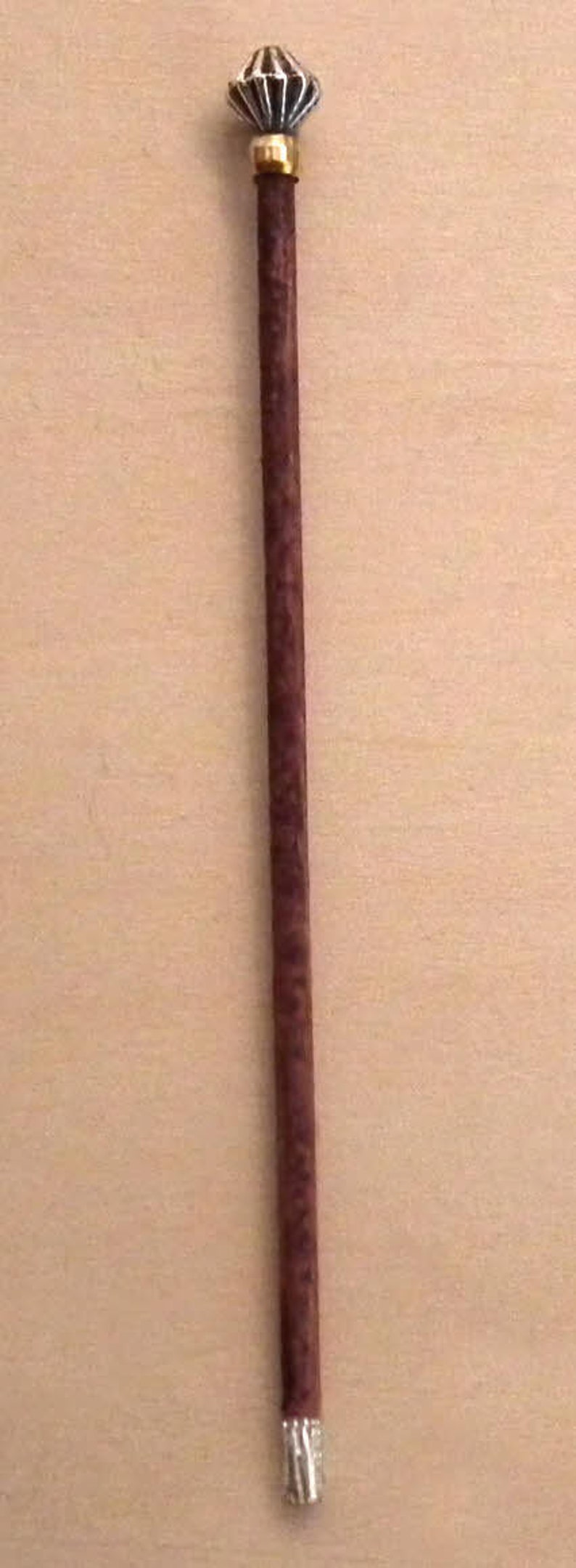 May include: A brown wooden walking stick with a silver and gold decorative top.