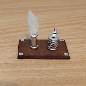 May include: A miniature wooden desk with a silver inkwell and a quill pen holder. The desk has a dark brown finish and silver accents.