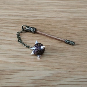 May include: A small, brown, spiked ball attached to a chain and a wooden stick with a metal tip. The ball is made of woven material and has silver-colored spikes.