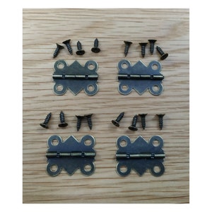 May include: Four antique brass butterfly hinges with eight matching screws. The hinges are arranged in two pairs on a wooden surface.