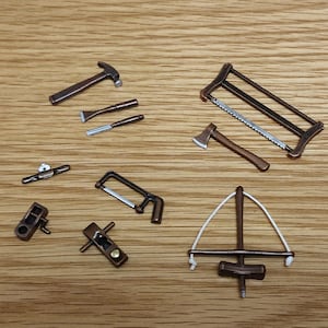 May include: A set of miniature woodworking tools, including a hammer, saw, axe, chisel, plane, and a bow drill. The tools are made of metal and wood and have a rustic, antique finish.