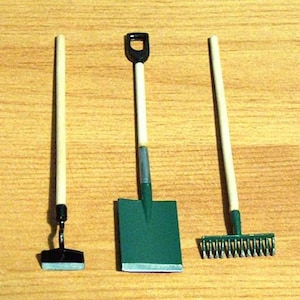 May include: A set of three miniature gardening tools: a green shovel, a rake with metal tines, and a small hoe with a wooden handle.