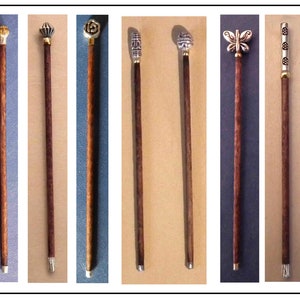 May include: Eight decorative walking sticks with different metal tops. The tops feature a variety of designs, including a flower, a butterfly, and geometric patterns. The sticks are all made of dark wood.