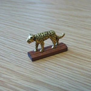 May include: A gold-coloured figurine of a leopard standing on a wooden base. The leopard is detailed with spots.