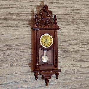 May include: A brown wooden wall clock with a gold face and a pendulum. The clock has a horse figure on top and ornate details.