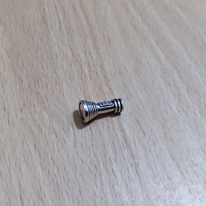 May include: A silver-coloured flashlight charm with a textured design. The charm is small and compact, ideal for adding a touch of style to a keychain or bracelet.