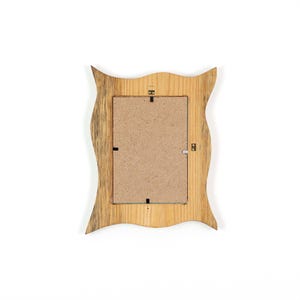 Pu&ograve; includere: Vista posteriore di una cornice in legno con un design a bordo ondulato unico. La cornice &egrave; realizzata in legno chiaro con accenti pi&ugrave; scuri e strutturati. Il retro include un inserto di cartone e ferramenta per appendere.