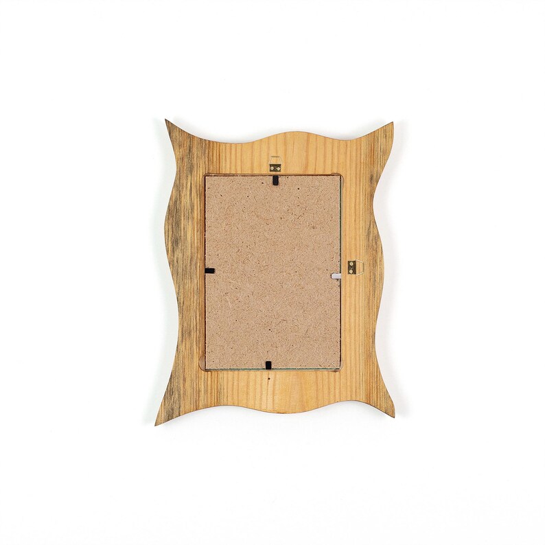 Pu&ograve; includere: Vista posteriore di una cornice in legno con un design a bordo ondulato unico. La cornice &egrave; realizzata in legno chiaro con accenti pi&ugrave; scuri e strutturati. Il retro include un inserto di cartone e ferramenta per appendere.