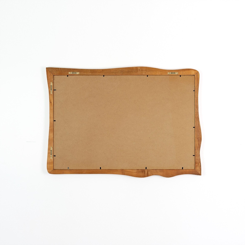 Pu&ograve; includere: Vista posteriore di una cornice rettangolare in legno con bordo ondulato. La cornice &egrave; di colore marrone chiaro e ha un retro in cartone. Clip metalliche e ferramenta per appendere sono visibili sul retro.