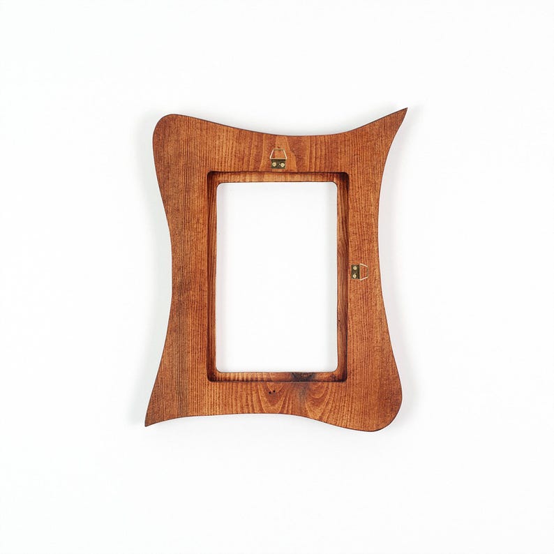 May include: A wooden picture frame with a distinctive, curved design. The frame is a warm brown colour and has a rectangular aperture. Two metal hangers are attached to the back for wall mounting. The frame is empty.