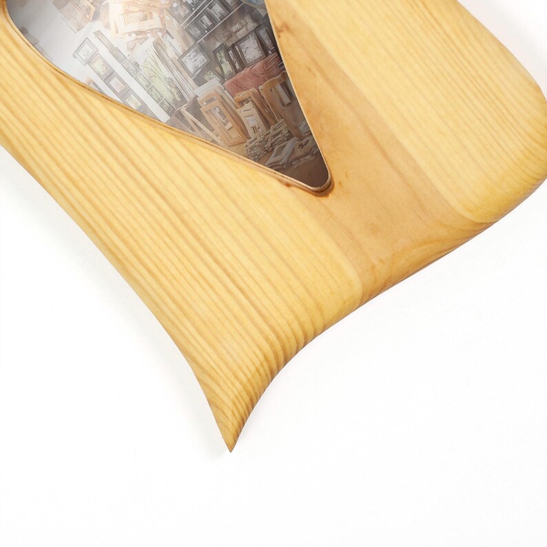 May include: A light-coloured wooden picture frame with a distinct, asymmetrical, pointed shape. The frame features a visible natural wood grain pattern and contains a photograph depicting a collection of various framed art pieces.