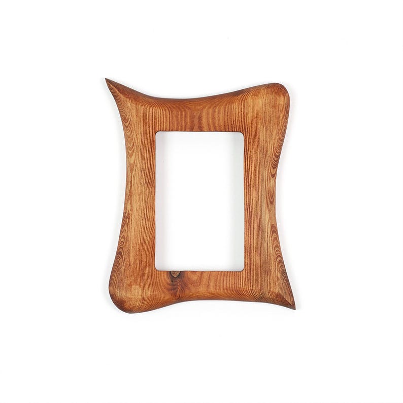 May include: A wooden picture frame with a distinctive, curved design. The frame is made of light brown wood with visible grain and a rectangular aperture. The frame's edges curve outwards, creating an elegant, organic shape.