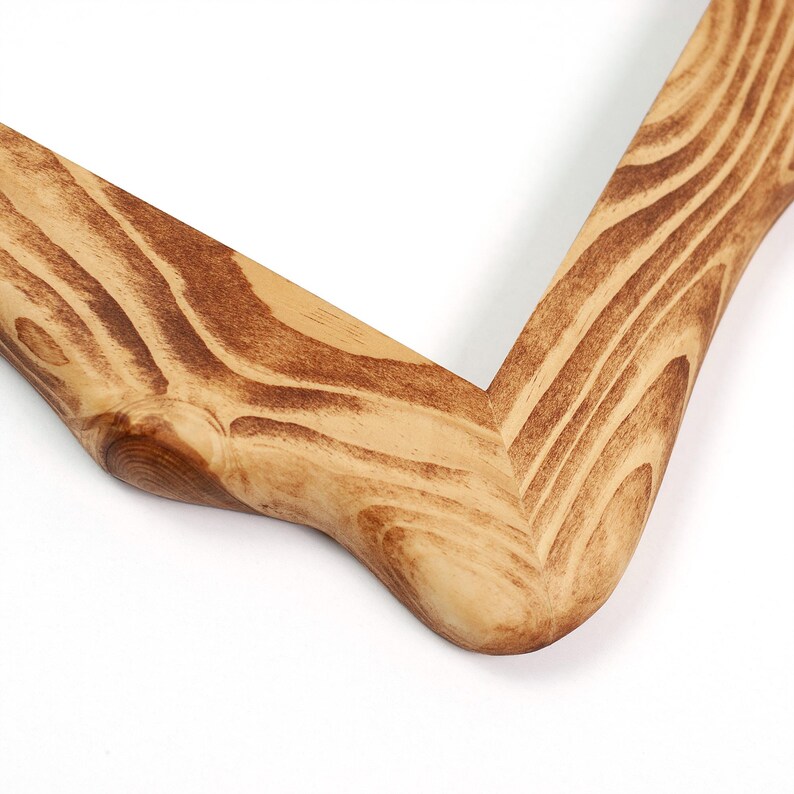 K&ouml;nnte beinhalten: Nahaufnahme einer Ecke eines Holzfotorahmens. Der Rahmen besteht aus hellem Holz mit einem nat&uuml;rlichen Maserungsmuster und dunkleren braunen Streifen. Die Ecke ist abgerundet und glatt, mit nat&uuml;rlichem Finish.