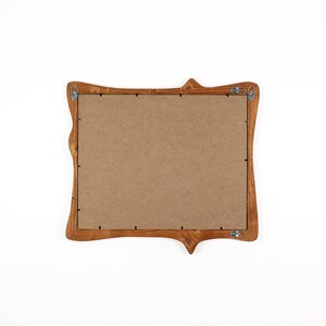 Pu&ograve; includere: Una cornice in legno con un design decorativo e curvo. La cornice &egrave; tinta con un caldo colore marrone e ha un retro in cartone. Le grucce in metallo sono attaccate sul retro per il montaggio a parete. La cornice &egrave; vuota.
