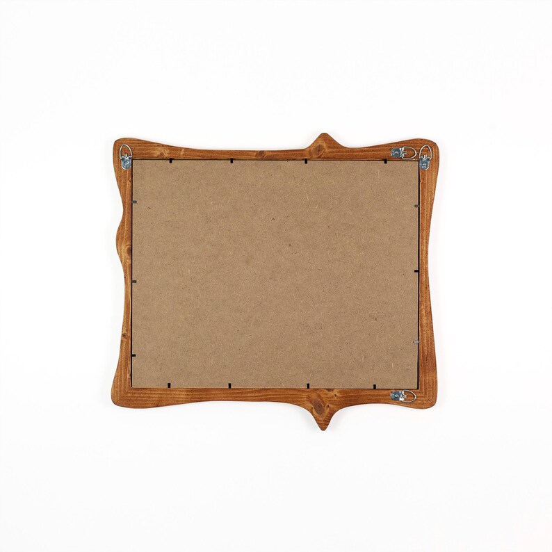 Pu&ograve; includere: Una cornice in legno con un design decorativo e curvo. La cornice &egrave; tinta con un caldo colore marrone e ha un retro in cartone. Le grucce in metallo sono attaccate sul retro per il montaggio a parete. La cornice &egrave; vuota.