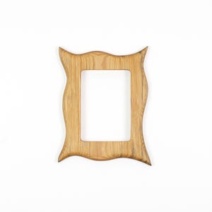 Pu&ograve; includere: Una cornice in legno marrone chiaro con apertura rettangolare. La cornice presenta un design ondulato unico con bordi appuntiti in alto e in basso. La venatura del legno &egrave; visibile, aggiungendo consistenza. Progettata per una foto rettangolare.