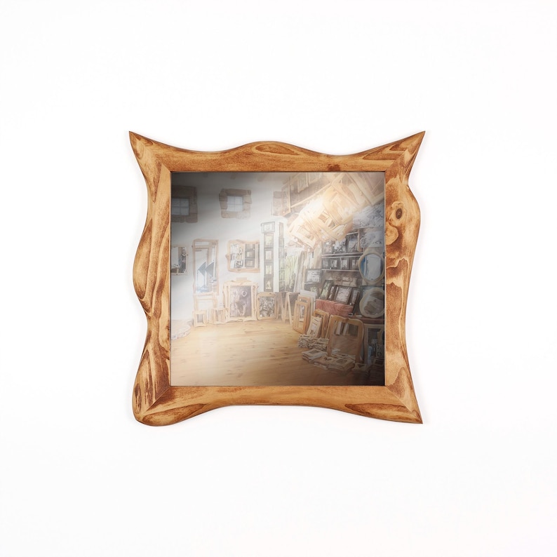 May include: A square wooden mirror with a unique, organic frame. The frame is a warm, light brown color with a natural wood grain texture. The mirror reflects a room filled with artwork.