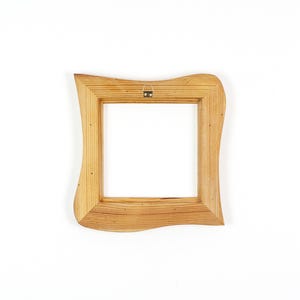 Pode incluir: Uma moldura quadrada de madeira com um acabamento natural de gr&atilde;o de madeira castanho claro. A moldura apresenta um design exterior ondulado e irregular e inclui um pequeno suporte met&aacute;lico para pendurar fixado no centro do bordo superior.