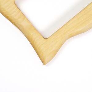 Pu&ograve; includere: Una cornice in legno di colore chiaro con una finitura liscia e lucida e un distinto motivo a venature naturali. La cornice presenta un giunto angolare a forma di V, che mette in mostra le tonalit&agrave; beige chiaro e crema del legno in un design pulito.