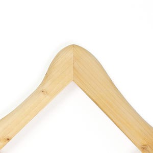 K&ouml;nnte beinhalten: Ein heller Holzkleiderb&uuml;gel mit einer glatten Oberfl&auml;che und nat&uuml;rlicher Maserung. Der B&uuml;gel hat ein geschwungenes, gew&ouml;lbtes Oberteil mit einer zentralen Verbindungsstelle, an der die beiden abgewinkelten Arme aufeinandertreffen.