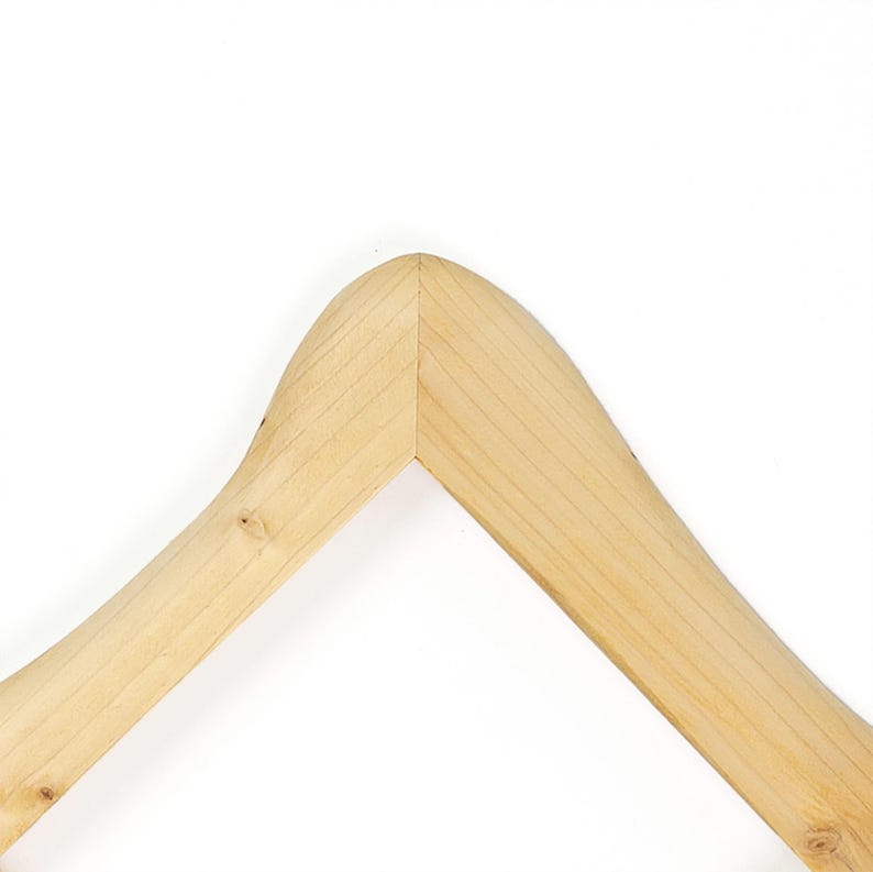 K&ouml;nnte beinhalten: Ein heller Holzkleiderb&uuml;gel mit einer glatten Oberfl&auml;che und nat&uuml;rlicher Maserung. Der B&uuml;gel hat ein geschwungenes, gew&ouml;lbtes Oberteil mit einer zentralen Verbindungsstelle, an der die beiden abgewinkelten Arme aufeinandertreffen.