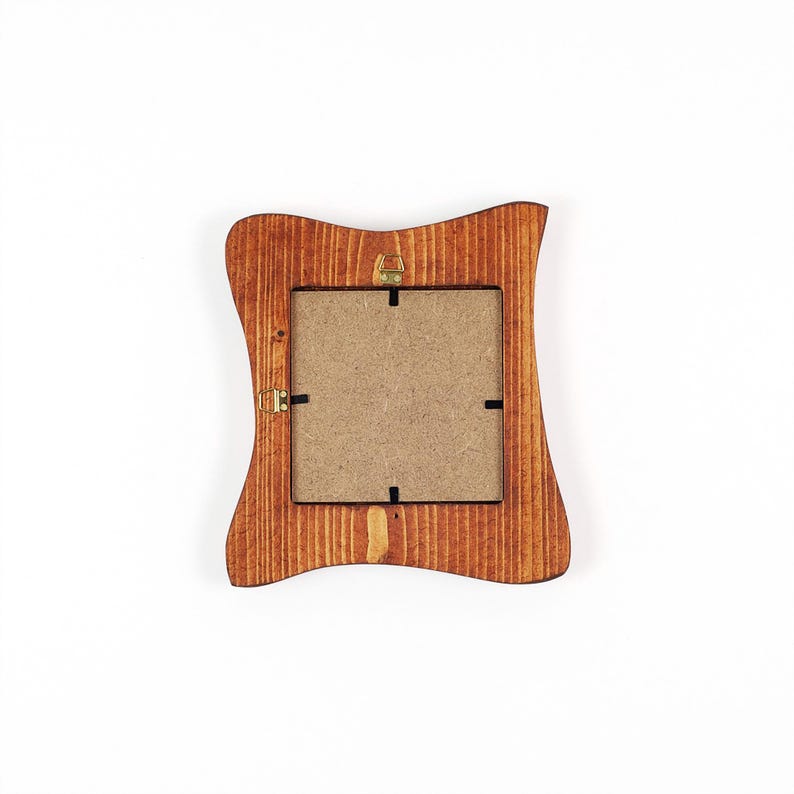 May include: A square wooden picture frame with a wavy, contoured outer edge and a natural brown wood grain finish. The back of the frame features a tan fiberboard backing secured by four metal clips and a single gold-toned metal hanging bracket.