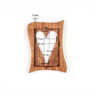 May include: A wooden picture frame with a heart-shaped cutout. The frame is brown with a wavy edge. The heart cutout measures 15 cm in height and 14 cm in width. The frame is 5 mm thick.