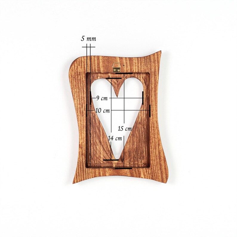 May include: A wooden picture frame with a heart-shaped cutout. The frame is brown with a wavy edge. The heart cutout measures 15 cm in height and 14 cm in width. The frame is 5 mm thick.