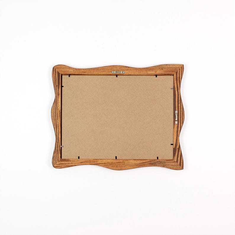 May include: A wooden picture frame with a wavy edge design. The frame is made of light brown wood and has a cardboard backing. The frame has metal hardware for hanging.
