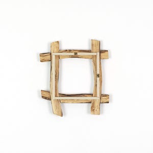 May include: A square picture frame constructed from four pieces of light brown natural wood with visible grain patterns. The frame features overlapping corners and a light-colored inner border with two small metal hanging brackets attached.