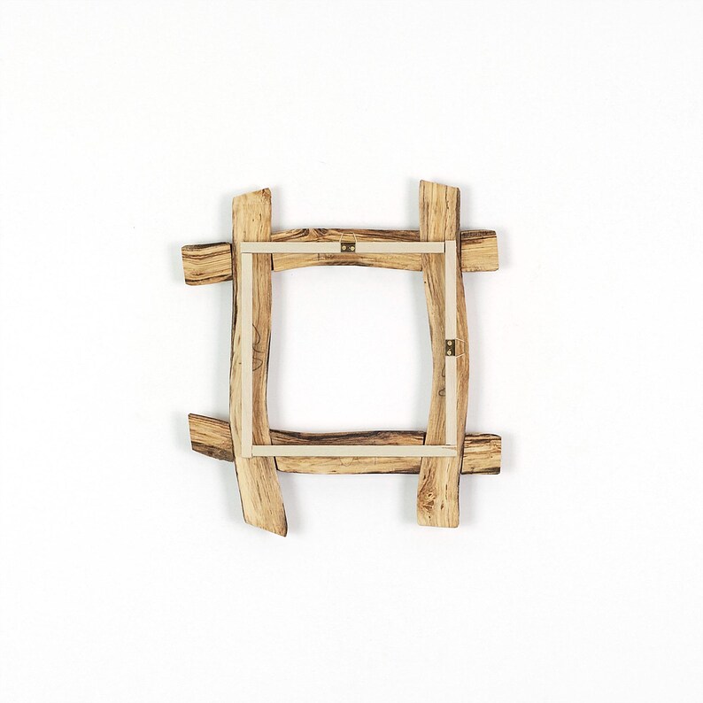 May include: A square picture frame constructed from four pieces of light brown natural wood with visible grain patterns. The frame features overlapping corners and a light-colored inner border with two small metal hanging brackets attached.