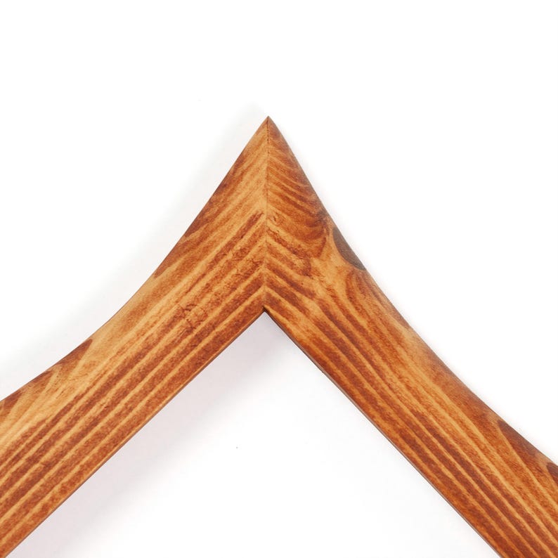 May include: Close-up of a wooden picture frame corner. The frame is made of light brown wood with visible grain and a smooth finish. The corner is precisely cut and joined, showcasing the craftsmanship of the frame.