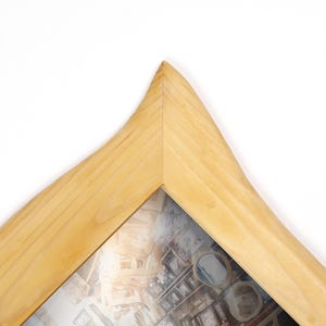 May include: A light-coloured wooden picture frame with a distinctive, curved design. The frame features a natural wood grain and a glass front, displaying a collage of images. The frame's corner is pointed, adding a unique touch to the overall aesthetic.