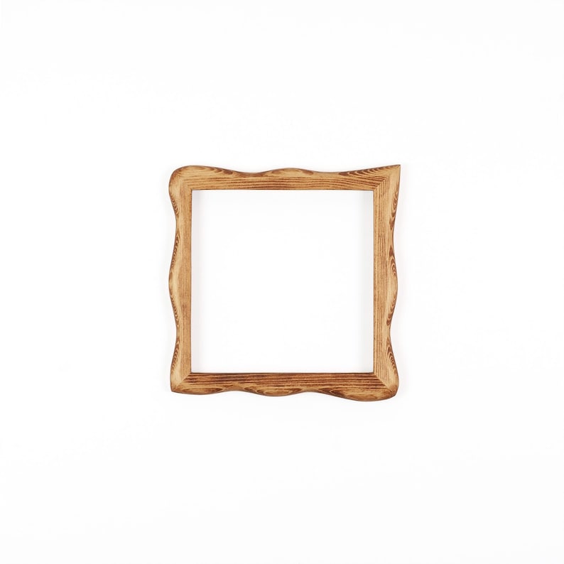 May include: A square wooden picture frame with a natural light brown finish and visible wood grain patterns. The frame features a distinct wavy, organic edge design on all four sides, surrounding a central empty square opening for display.