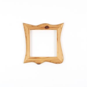 Puede incluir: Un marco de fotos cuadrado de madera con un acabado de veta de madera natural de color marr&oacute;n claro. El marco presenta un borde exterior ondulado y org&aacute;nico distintivo con nudos visibles en la veta, rodeando una abertura interior cuadrada.