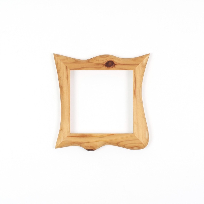 Puede incluir: Un marco de fotos cuadrado de madera con un acabado de veta de madera natural de color marr&oacute;n claro. El marco presenta un borde exterior ondulado y org&aacute;nico distintivo con nudos visibles en la veta, rodeando una abertura interior cuadrada.
