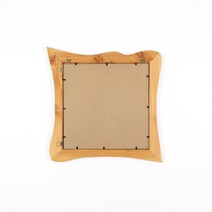 Peut inclure: Un cadre photo carr&eacute; en bois avec une finition naturelle en grain de bois brun clair et des bords ext&eacute;rieurs ondul&eacute;s et irr&eacute;guliers. Le dos du cadre pr&eacute;sente un panneau plat beige fix&eacute; par des clips m&eacute;talliques et deux attaches.
